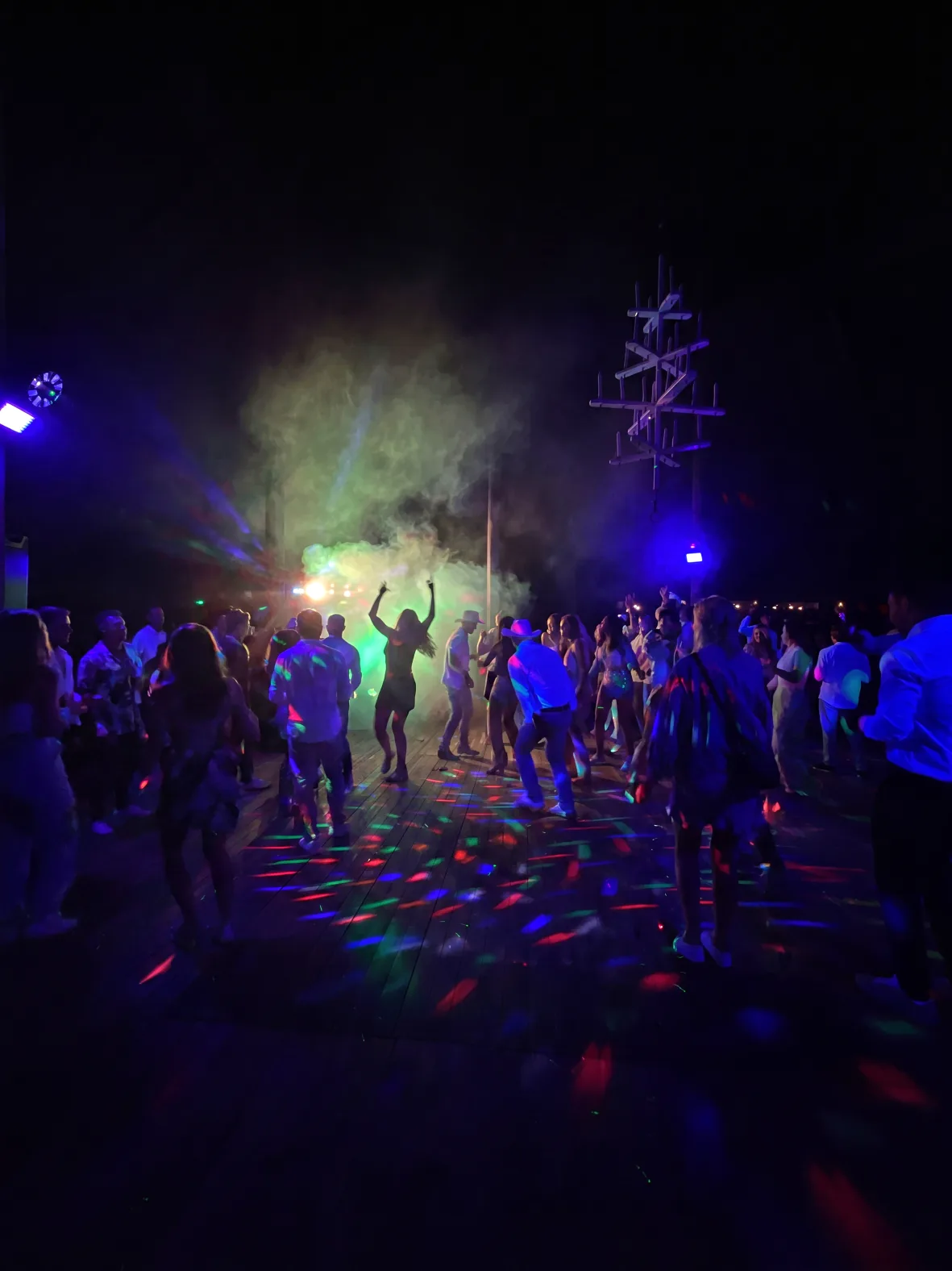 Gästerna dansar i grön rök på trädäcket medan färgade discoljus sveper över golvet.